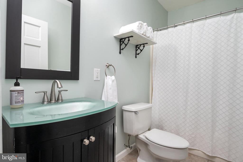 Bathroom with a black vanity, pale aqua glass countertop, and white patterned shower curtain.