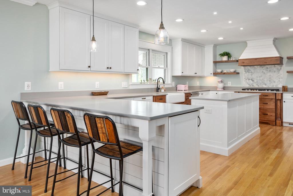 Bright kitchen with two large islands, white cabinetry, patterned backsplash, and hardwood floors.