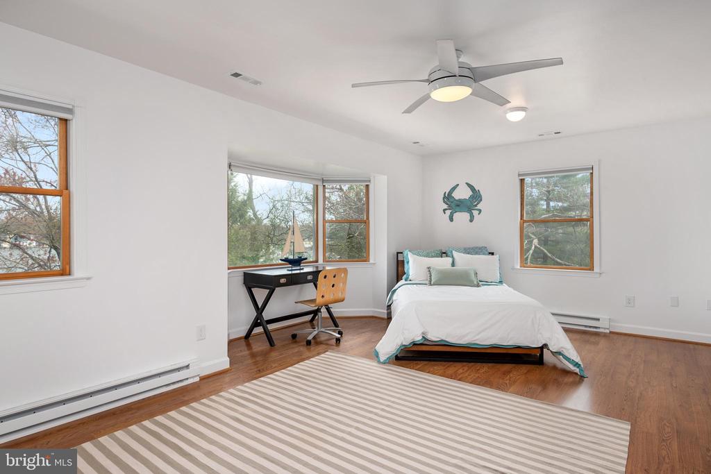 Bedroom with a bed, teal crab wall decor, desk by large windows, and striped rug.