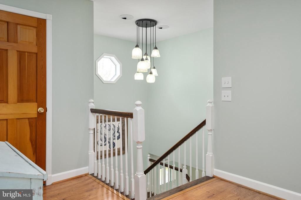 Upstairs landing with white stair railings, hardwood floors, and a cluster pendant light.