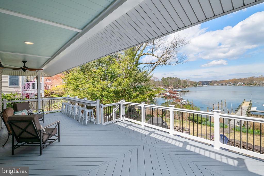 Covered waterfront deck with gray flooring, outdoor seating, and views of docks and boats.