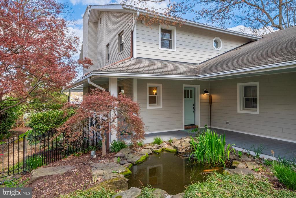 Two-story house with a covered porch, blue front door, and landscaped pond.