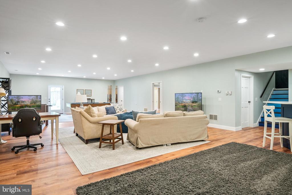 Furnished living and recreation room with beige sofas, hardwood floors, and a staircase with blue treads.