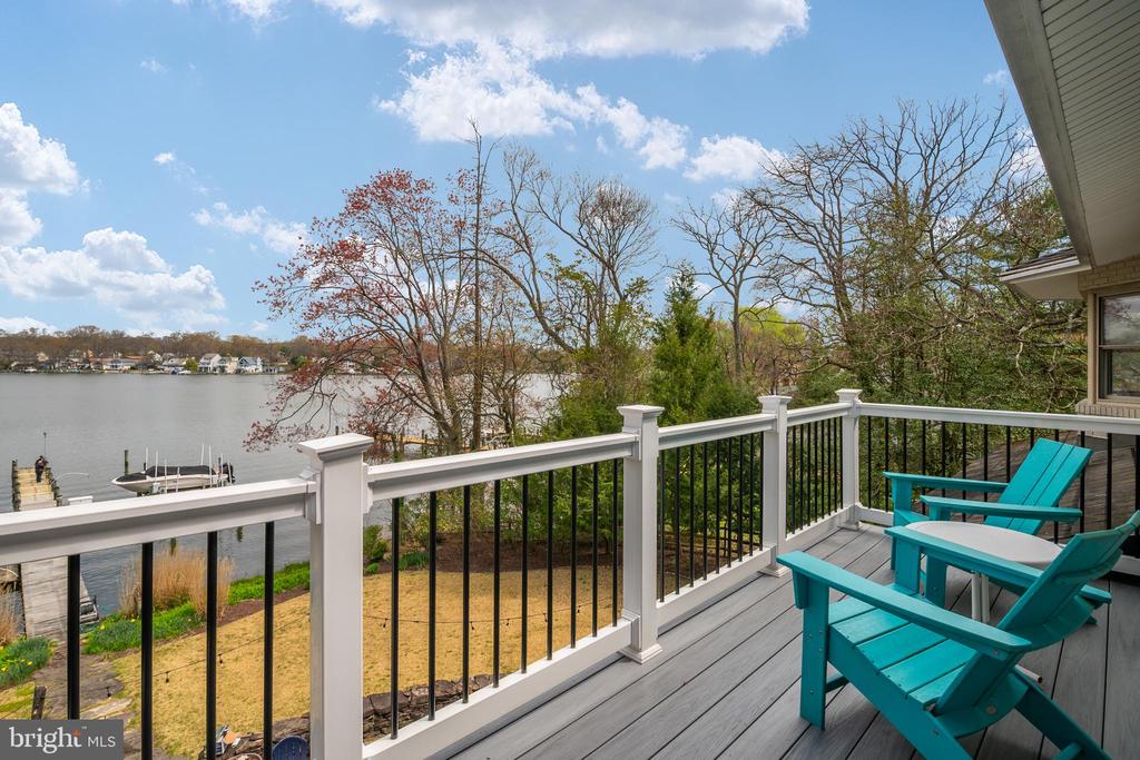 Deck with turquoise chairs overlooking calm water, a dock, and homes across the shore.