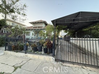 House behind a black metal fence and gate, with a covered carport on the right.
