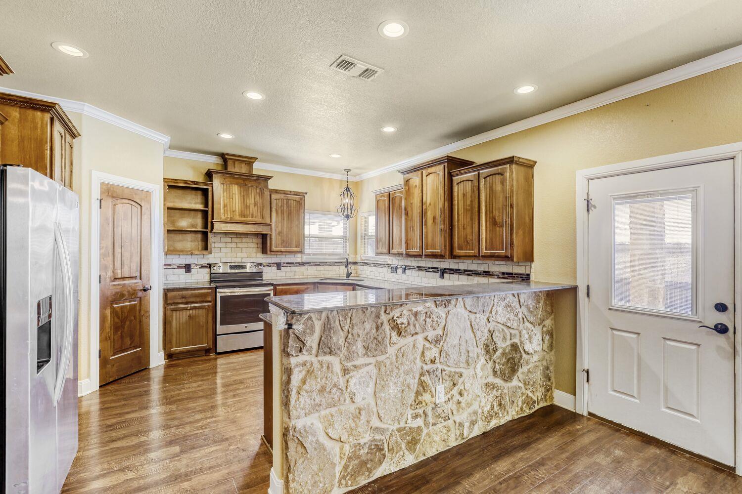 Kitchen with wood cabinets, stainless steel appliances, and a stone-front island.