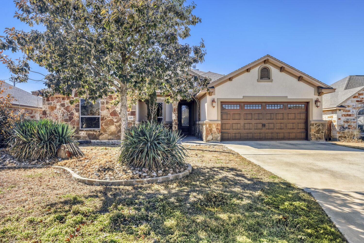 Stone-and-stucco home with a wide wooden garage door and landscaped front yard.