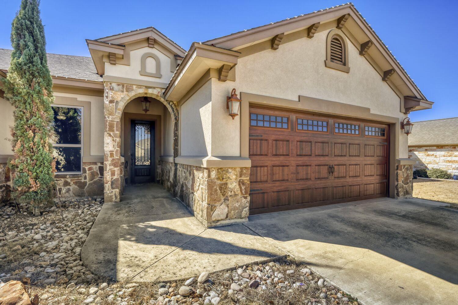 Stucco home with stone accents, an arched entry, and a large wooden garage door.