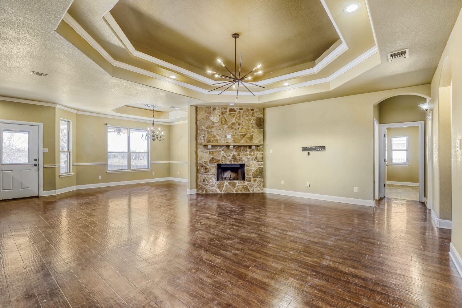 Vacant living room with a stone fireplace, tray ceiling, and starburst chandelier.
