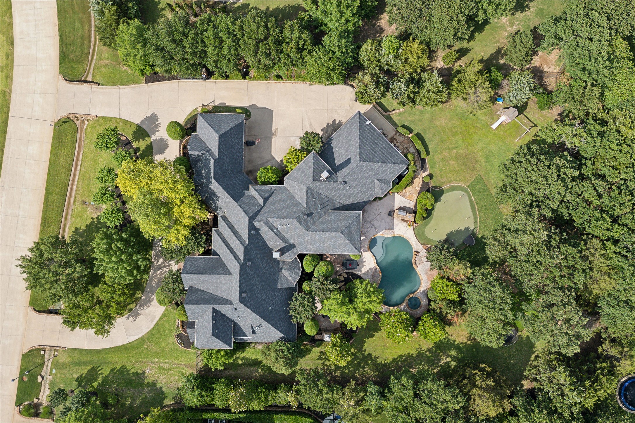 Aerial view of a large home with a swimming pool, landscaped grounds, and wooded lawn.