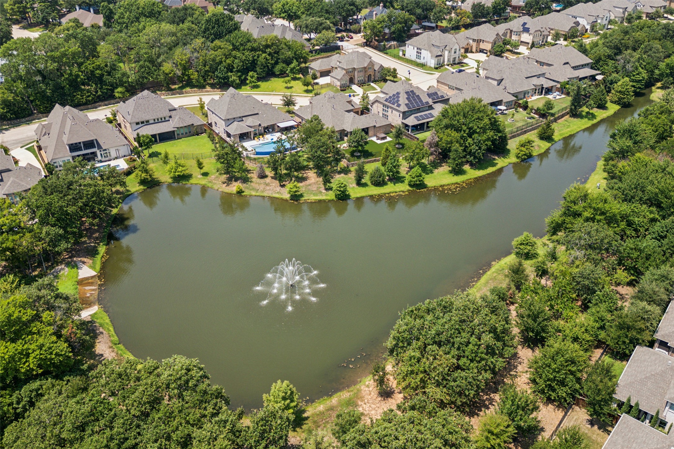 Aerial view of homes around a pond with a fountain and mature trees.