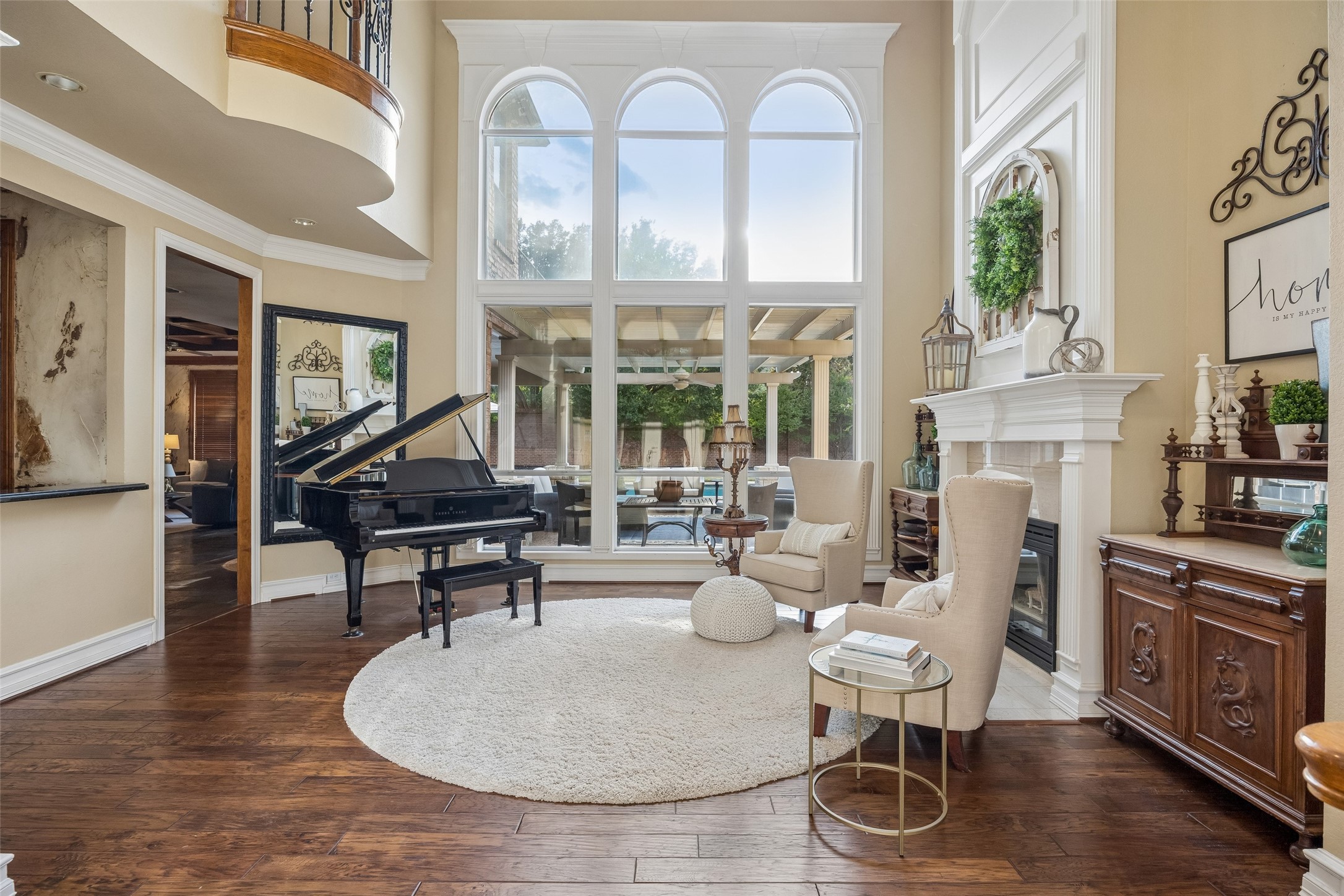 Living room with a grand piano, arched windows, cream armchairs, and a white fireplace.