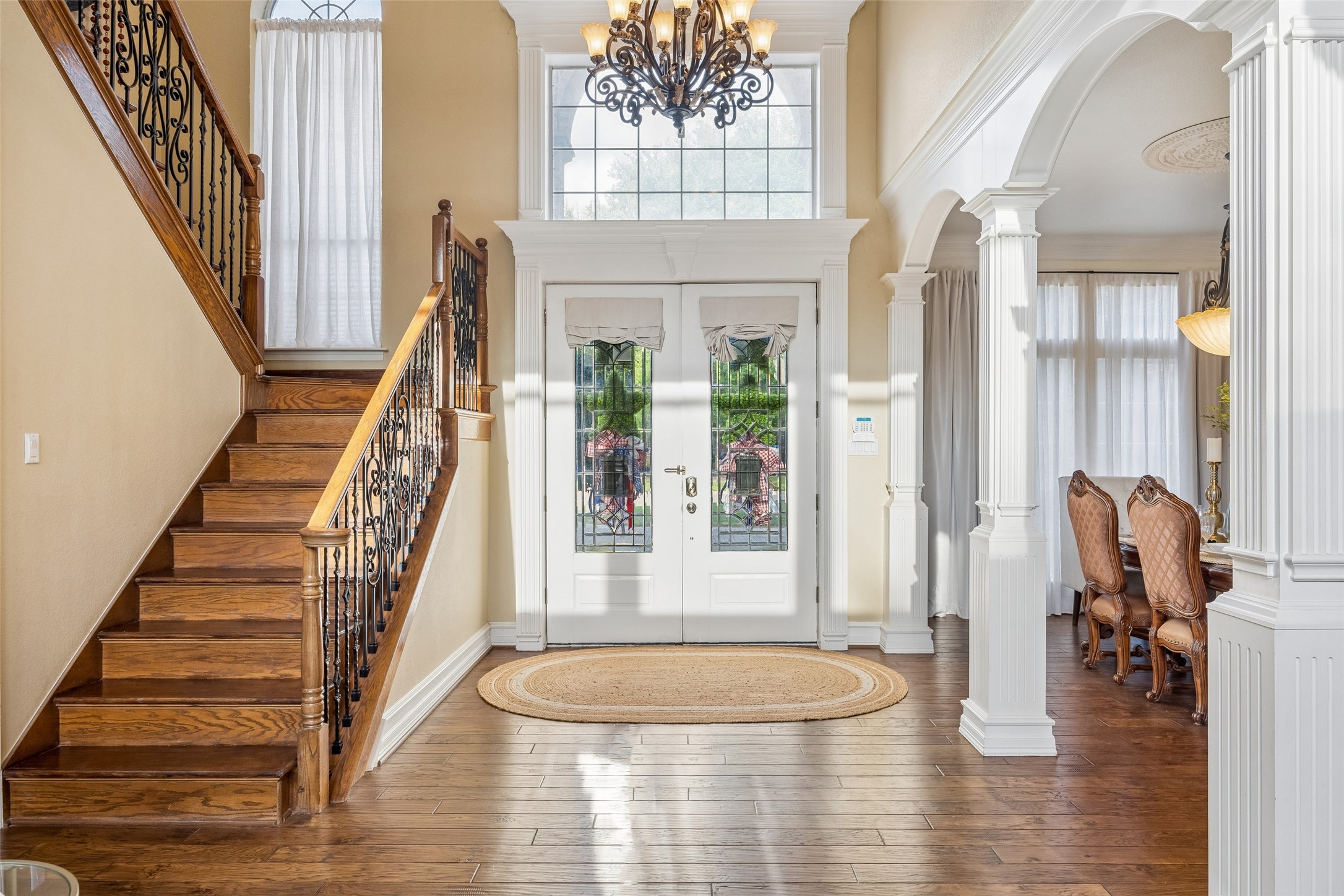 Foyer with a wood staircase, decorative glass double doors, and white arches opening to the dining room.