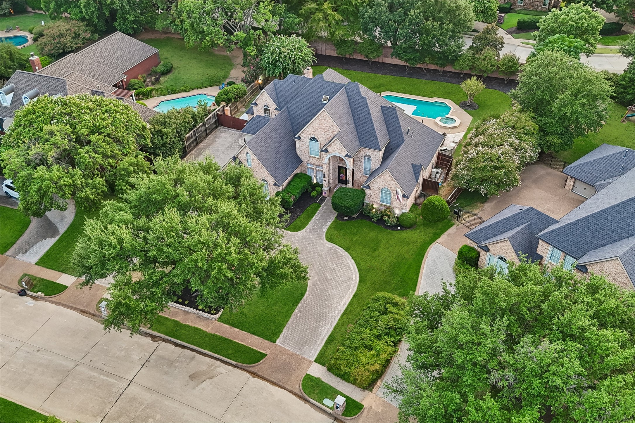Aerial view of a brick home with a curved driveway, landscaped grounds, and backyard pool.