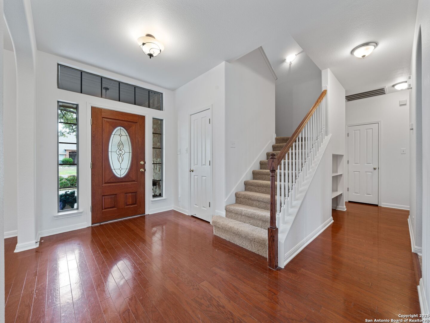 Entry foyer with glossy wood floors, an oval-glass front door, and a carpeted staircase.