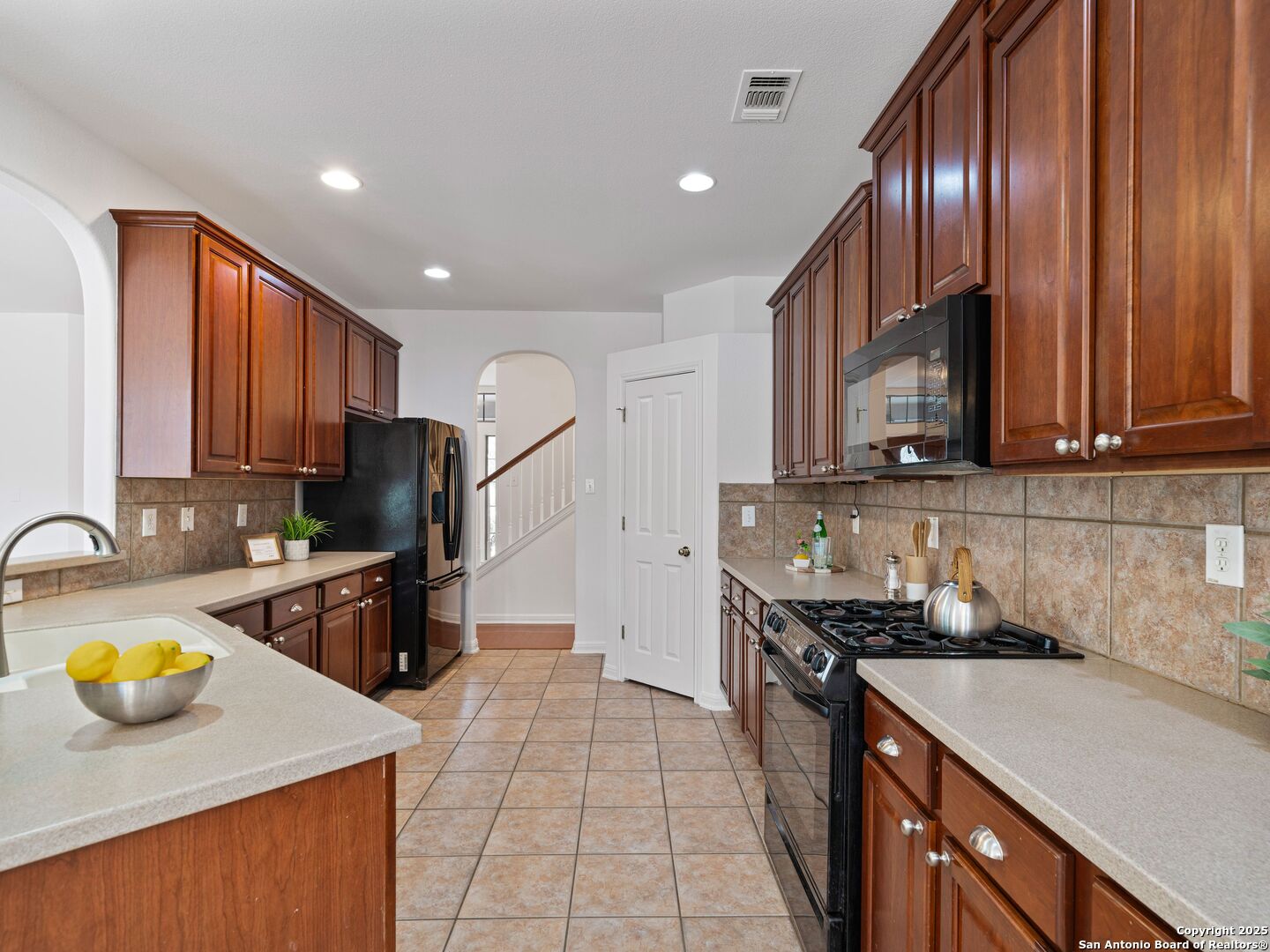 Kitchen with dark wood cabinetry, tiled backsplash, and a peninsula with a sink and bowl of lemons.