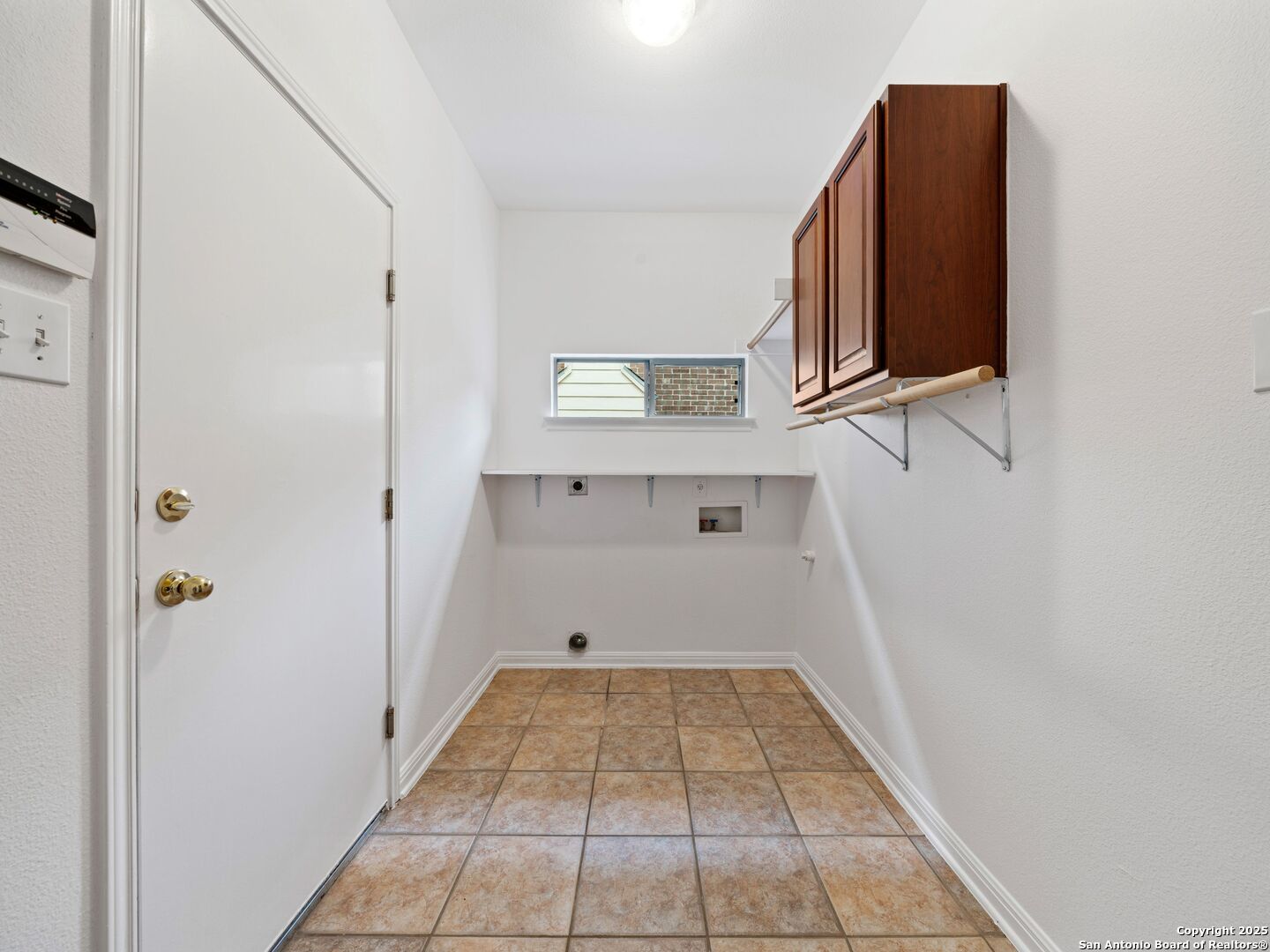 Empty laundry room with tan tile flooring, washer and dryer hookups, and dark wood cabinets.