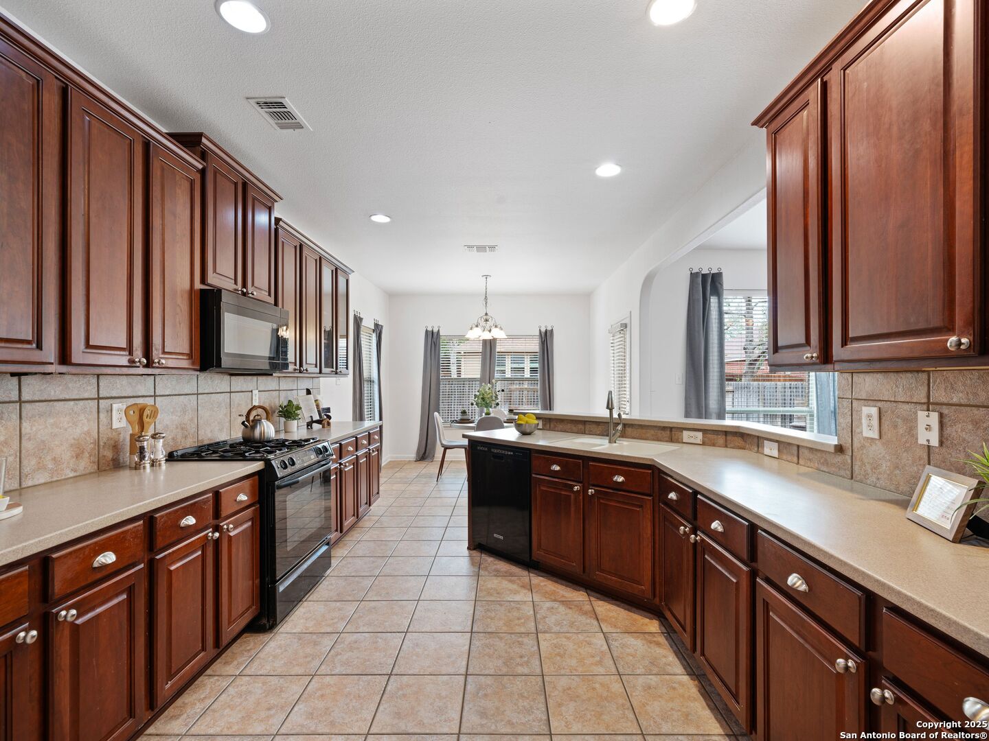 Kitchen with dark cherry cabinets, gas range, and a central sink island beside a dining area.
