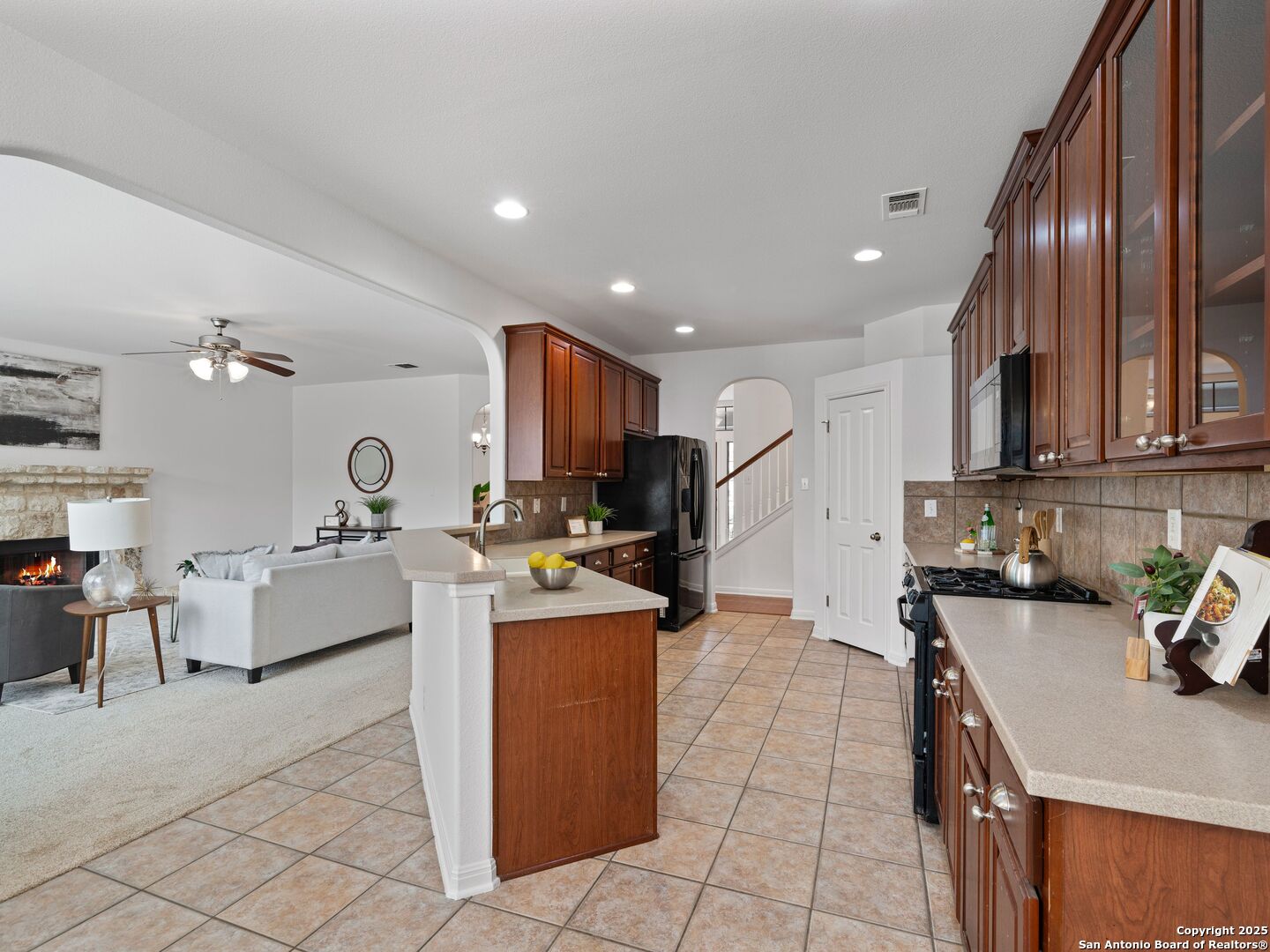 Open kitchen with dark wood cabinets and island adjoining a living room with a fireplace.