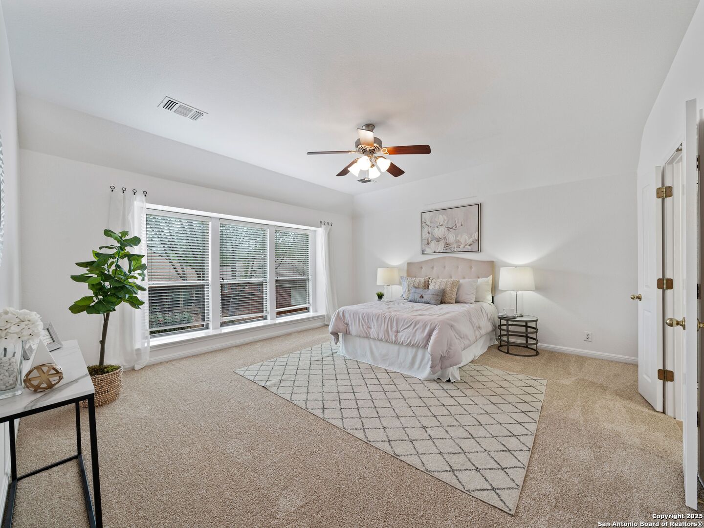 Staged bedroom with a tufted bed, broad windows with blinds, and a ceiling fan.