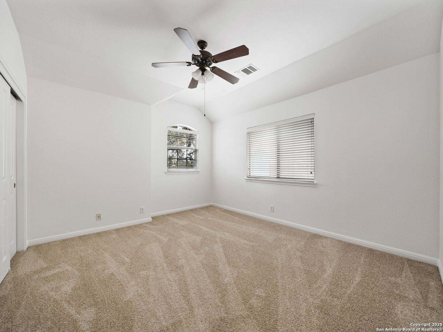 Empty carpeted bedroom with two windows and a dark wood ceiling fan.
