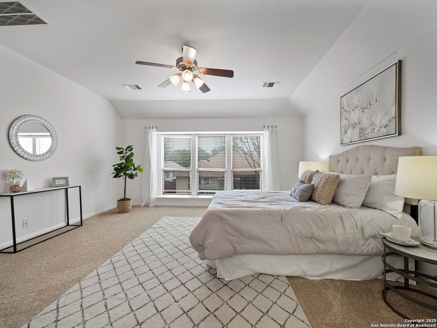 Staged bedroom with a large bed, tufted headboard, and wide window with blinds.