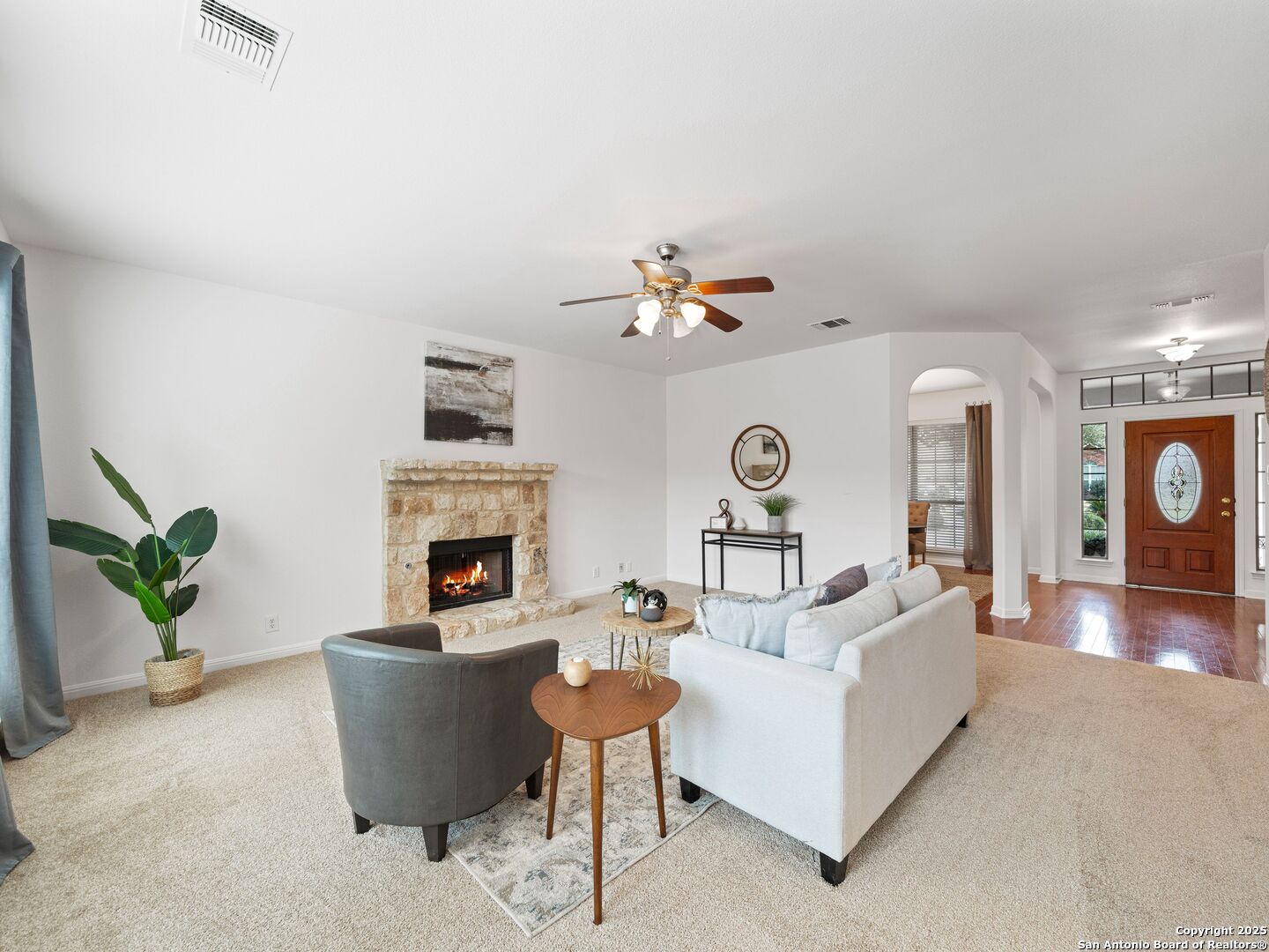 Living room with a stone fireplace, pale seating, and an arched opening to the front entry.