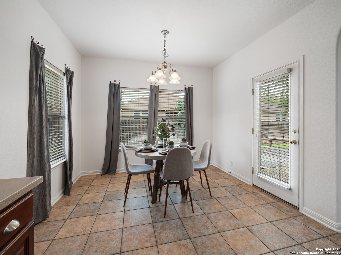 Dining room with a round table set for four, gray chairs, terracotta tile, and a chandelier.