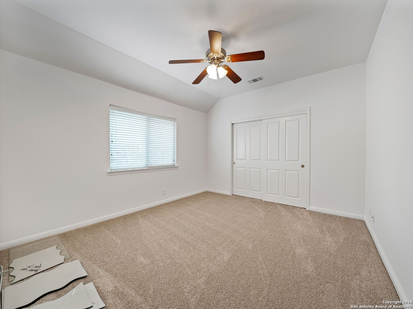Empty bedroom with beige carpet, sliding closet doors, window blinds, and a wood-blade ceiling fan.