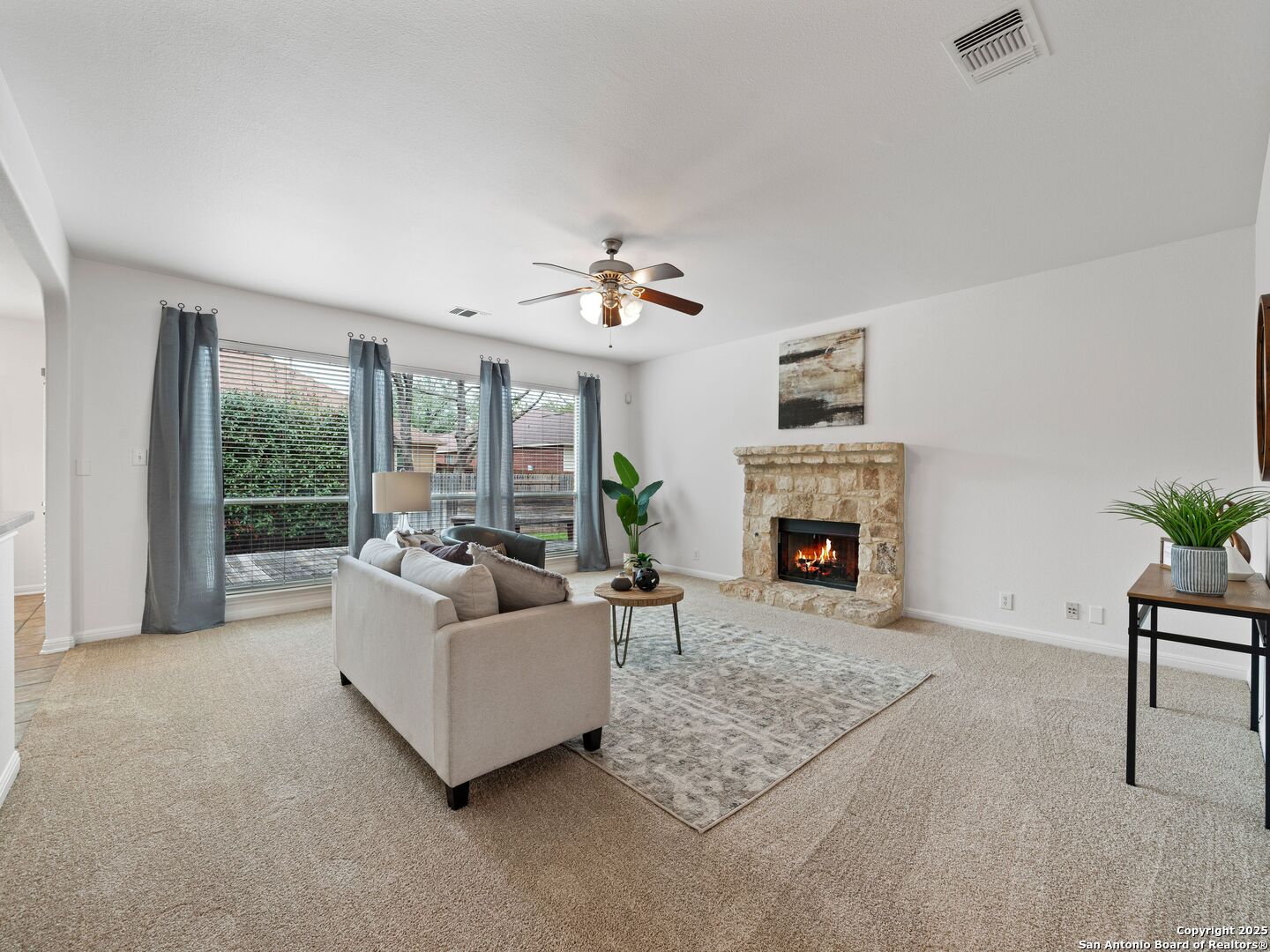 Living room with a stone fireplace, lit fire, and large curtained windows.