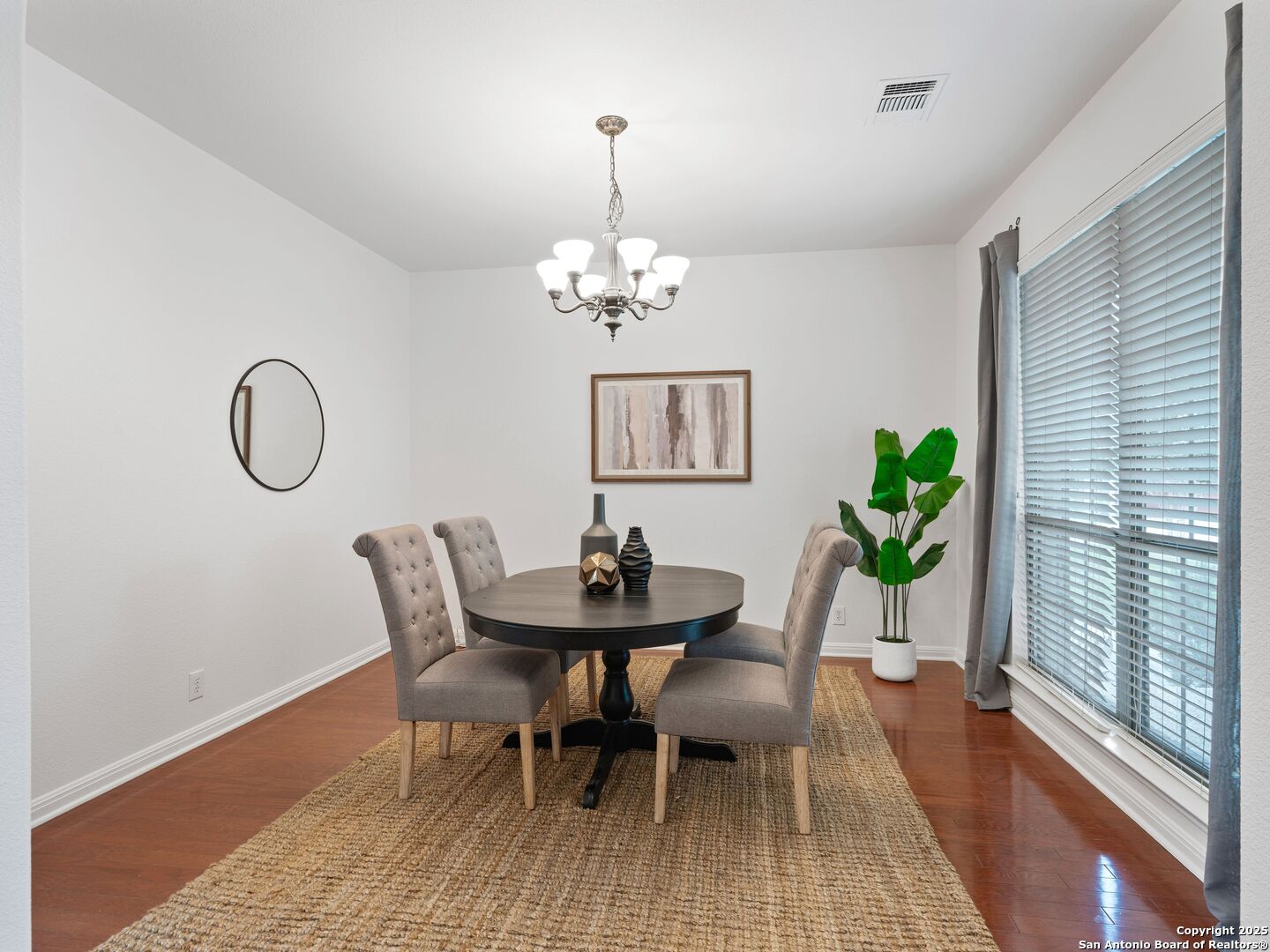 Staged dining room with a round table, gray chairs, and a large window with blinds.