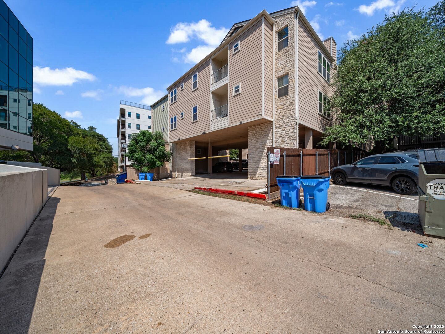 Multi-story apartment building with beige siding, stone accents, and parking beneath the structure.