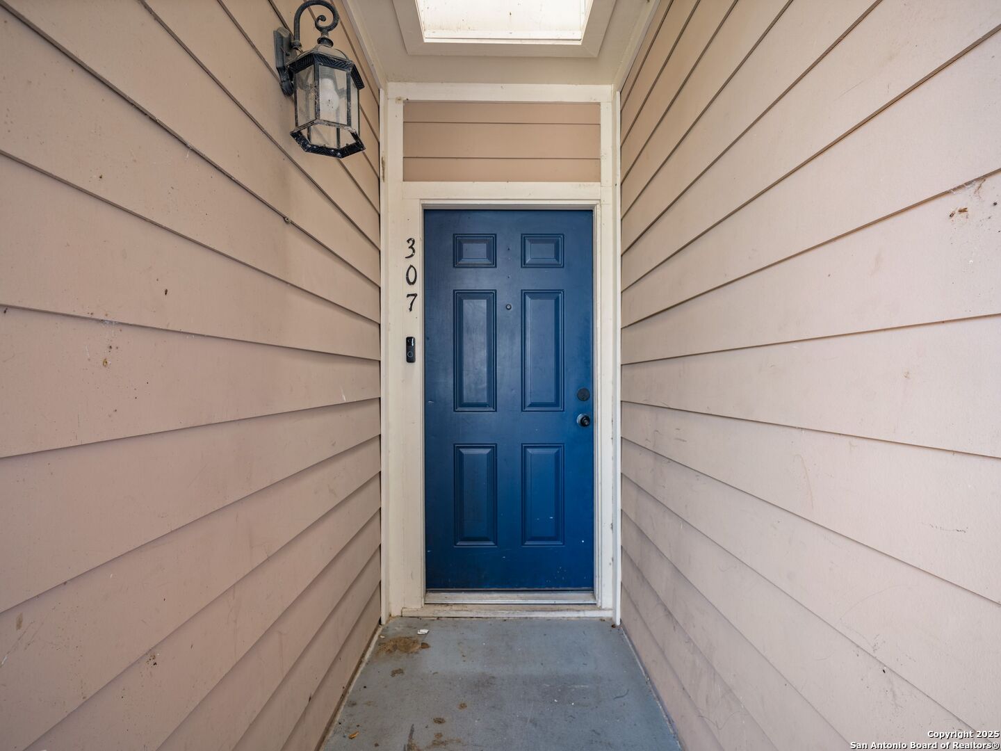 Apartment entrance with a blue paneled door, beige siding, and the number 307.
