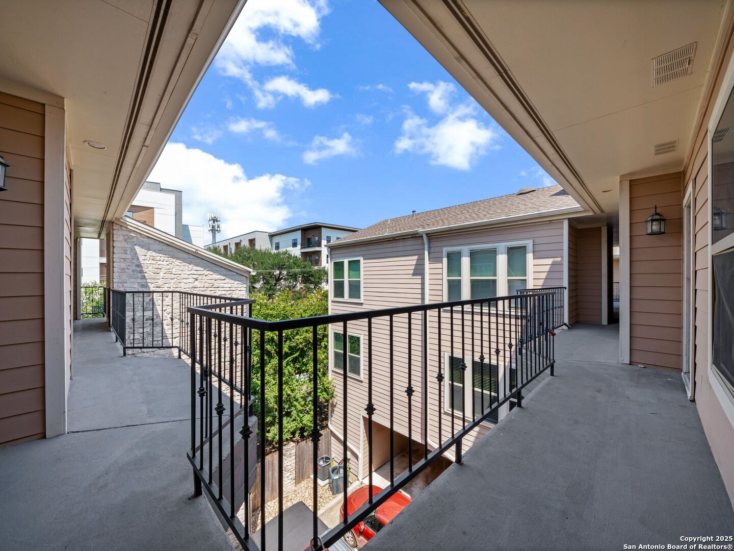 Covered apartment breezeway overlooking a leafy courtyard and neighboring building.