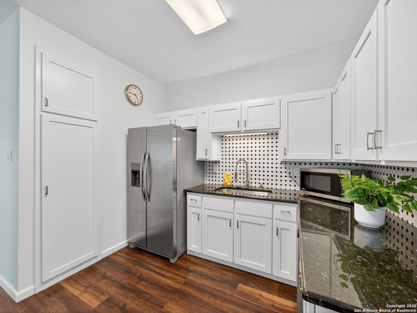 Bright kitchen with white cabinets, patterned backsplash, stainless steel appliances, and dark wood floors.