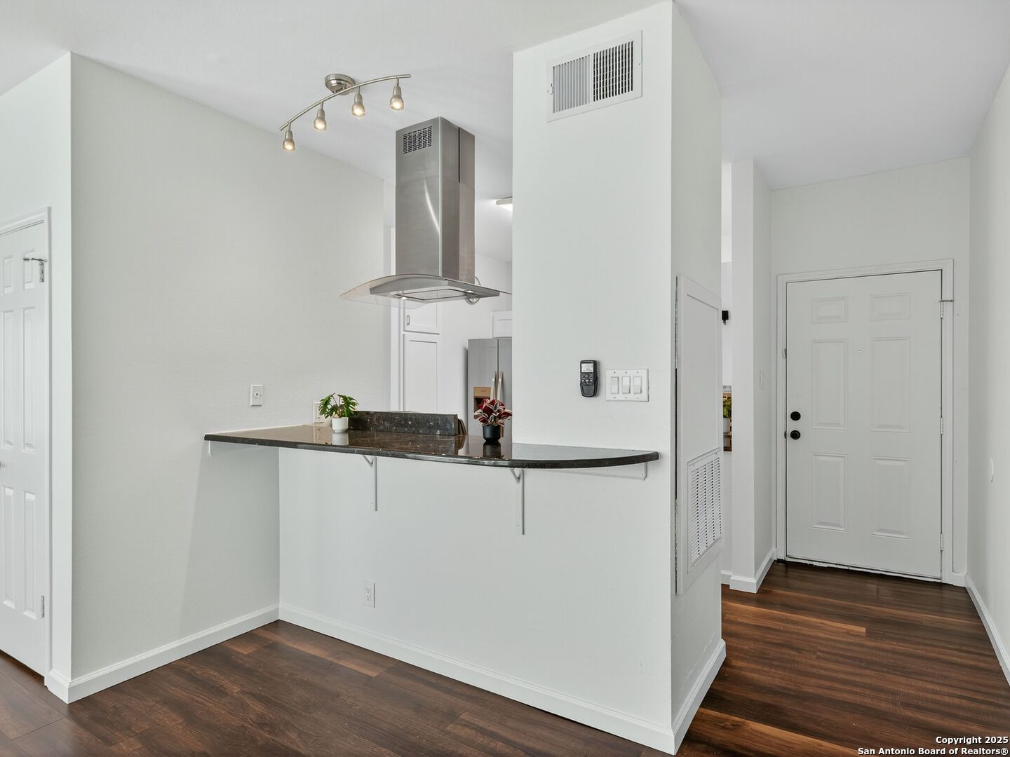 Open kitchen and entryway with a dark stone breakfast bar and stainless-steel range hood.