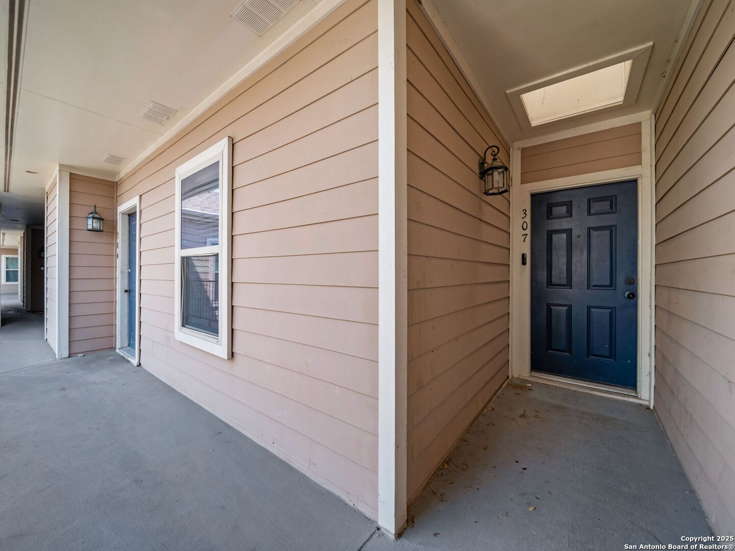 Apartment 307’s recessed blue entrance door along a covered corridor with tan siding.