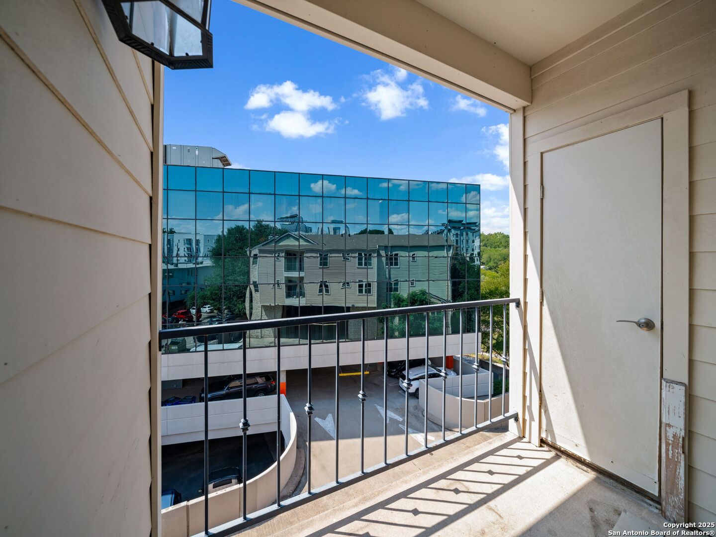 Apartment balcony overlooking a reflective glass office building and parking area.