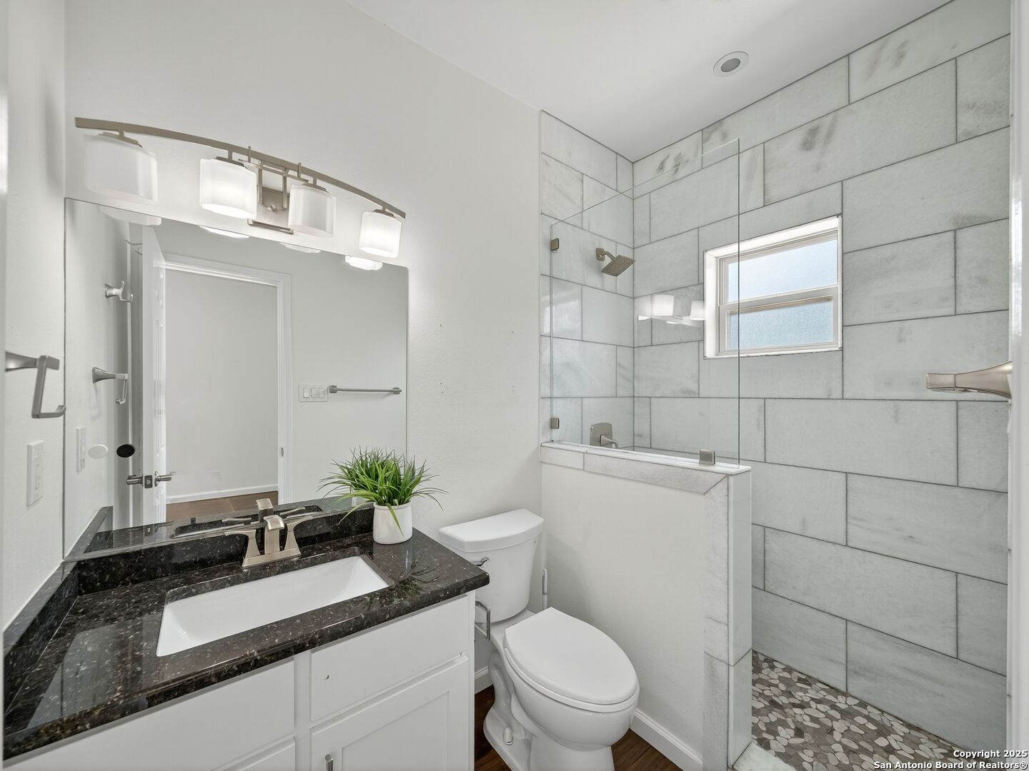 Bathroom with dark stone vanity, white tile shower, glass enclosure, and pebble floor.