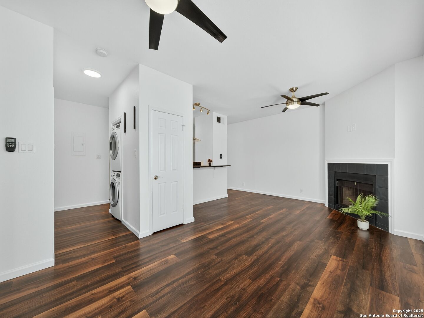 Open apartment living area with dark wood floors, a tiled fireplace, and stacked washer and dryer.