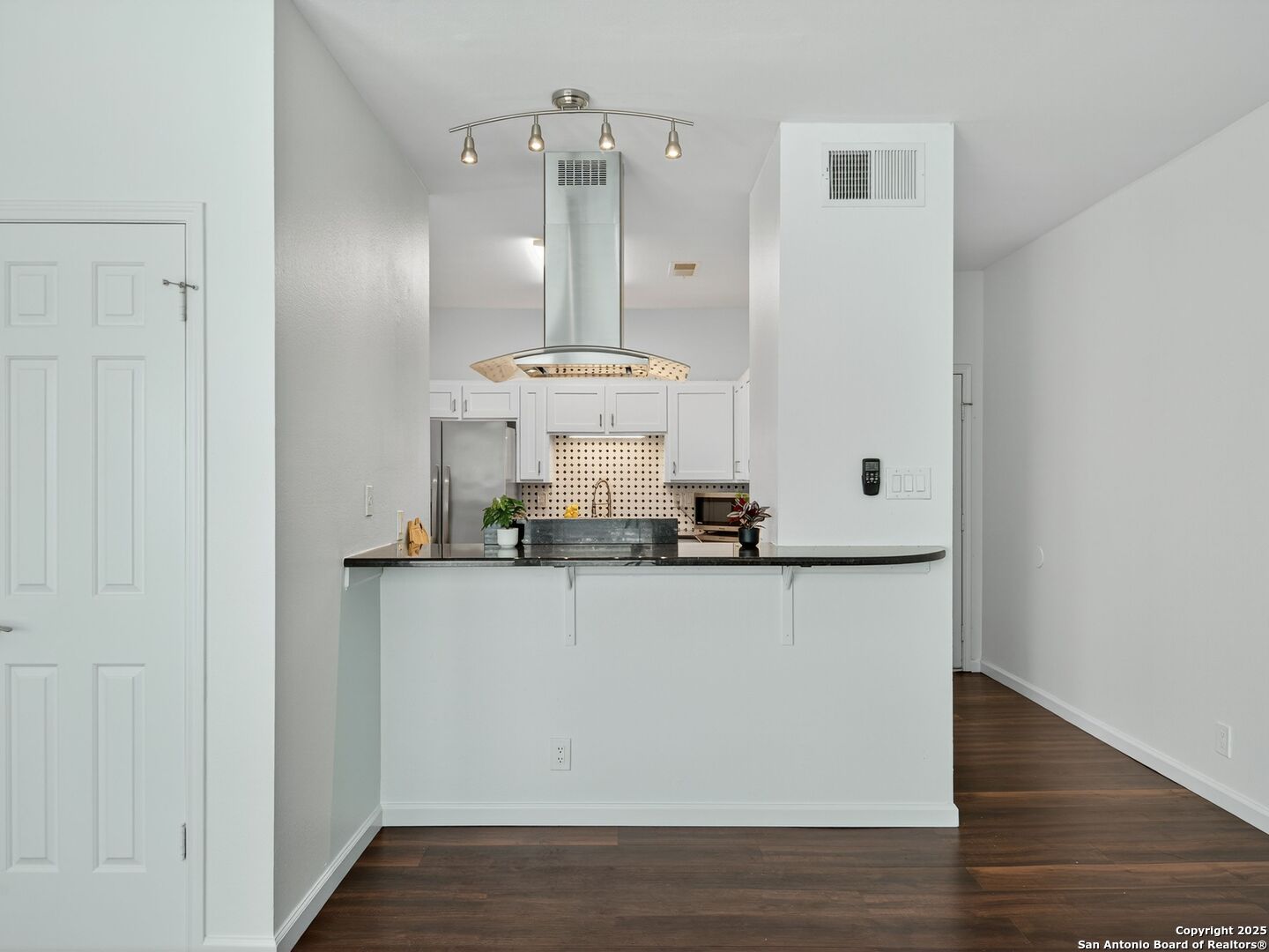 Kitchen with white cabinets, stainless-steel appliances, patterned backsplash, and a raised dark-countertop breakfast bar.