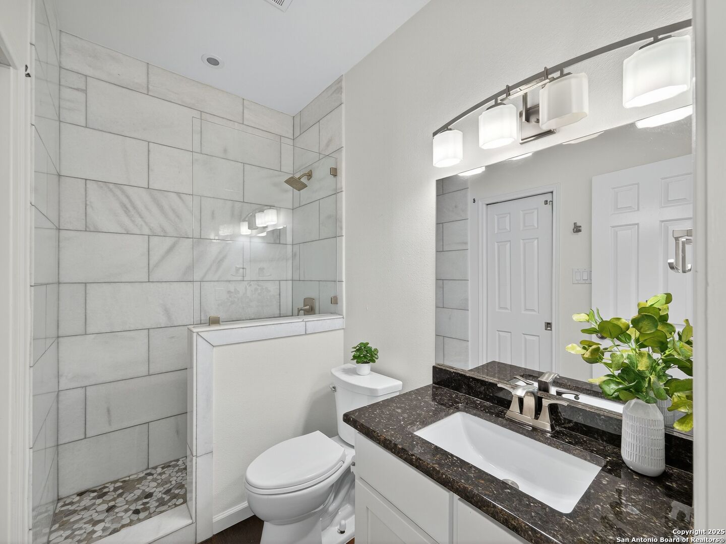 Bathroom with a tiled walk-in shower, pebble floor, and dark stone vanity countertop.