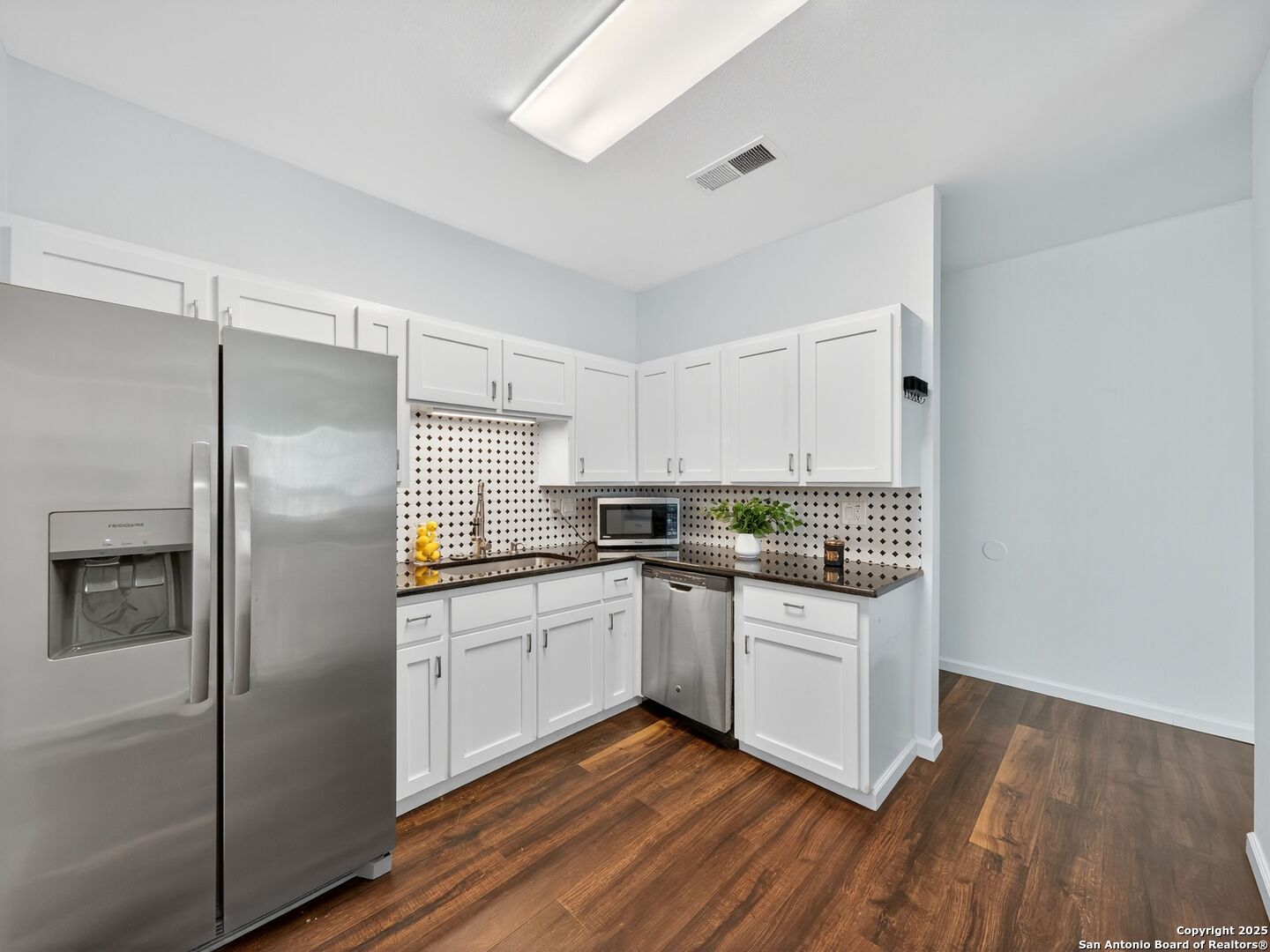 Apartment kitchen with white cabinets, patterned backsplash, stainless steel appliances, and wood floors.