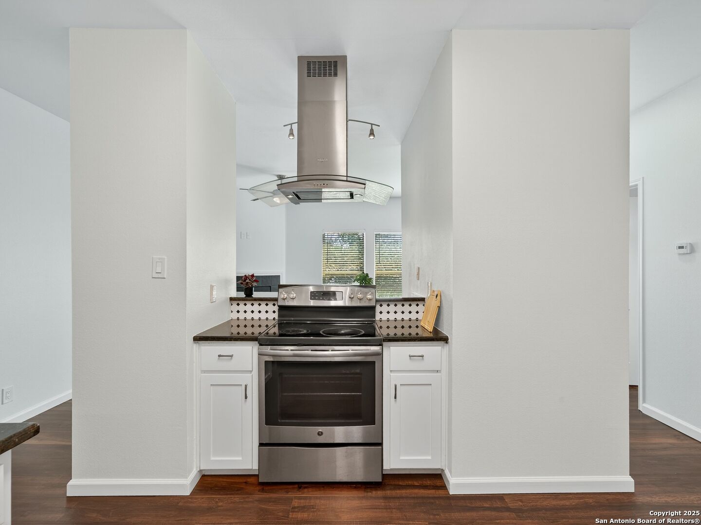 Apartment kitchen with stainless steel range, glass range hood, dark countertops, and diamond-pattern tile backsplash.