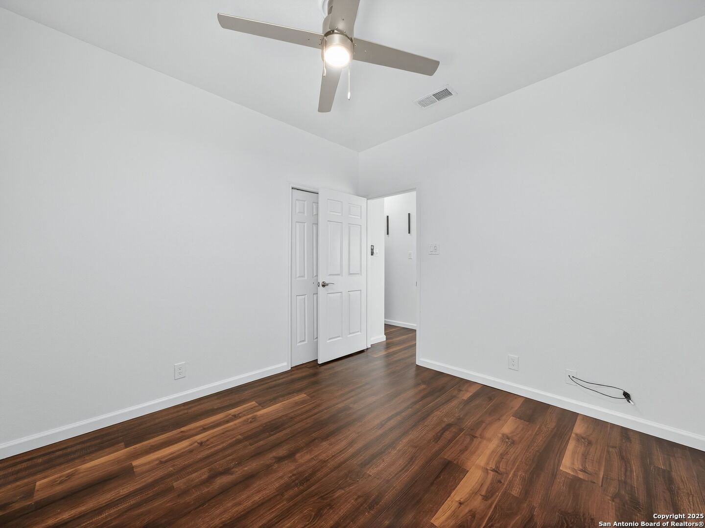 Empty room with dark wood flooring, white walls, and a ceiling fan.