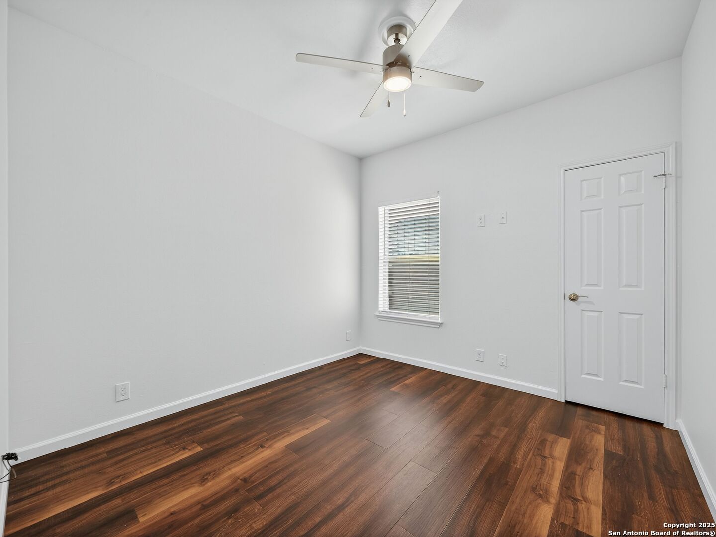 Empty room with dark wood flooring, a window with blinds, and a ceiling fan.