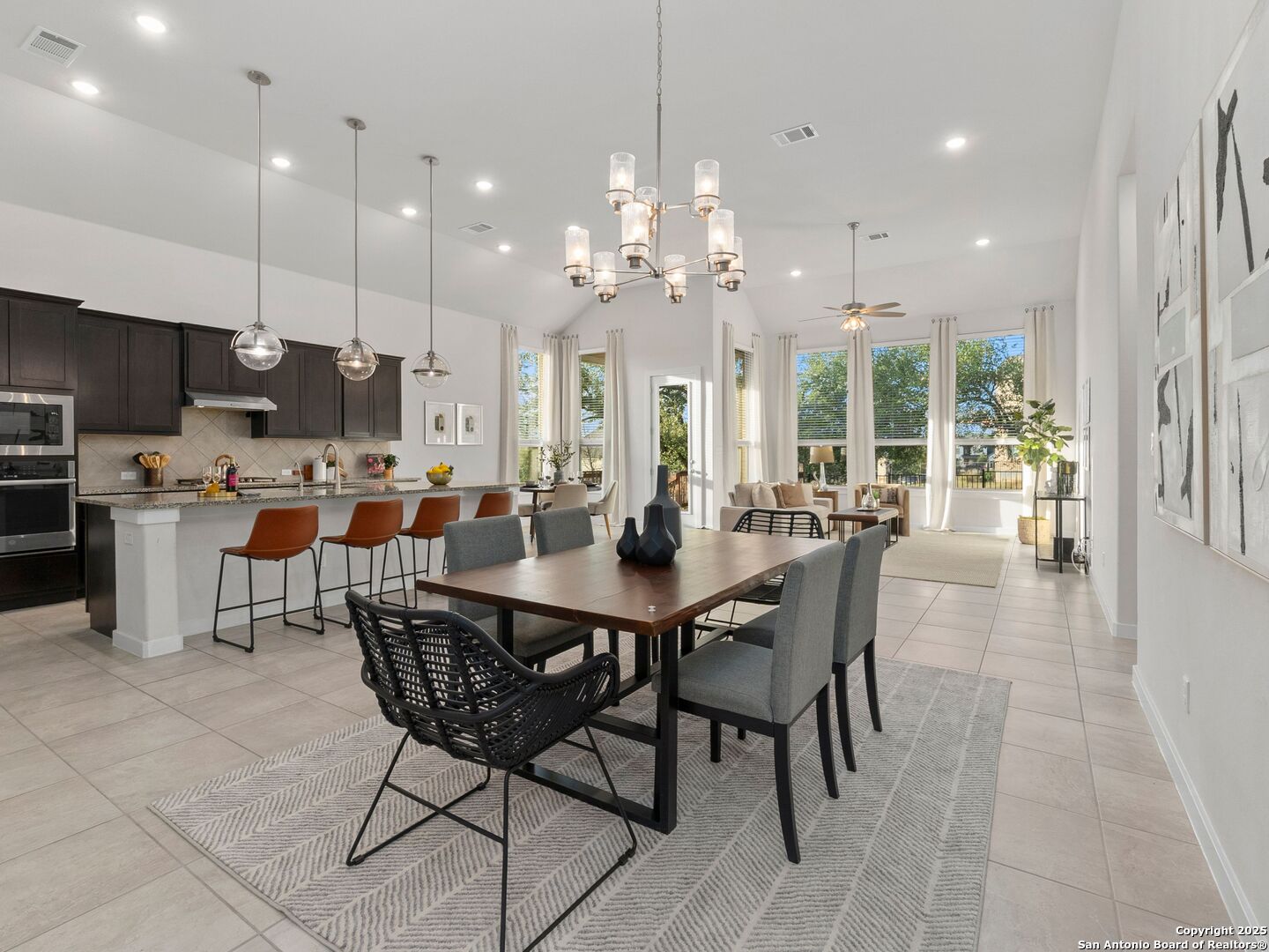 Open-plan kitchen and dining area with dark cabinets, a large table, and tall windows.
