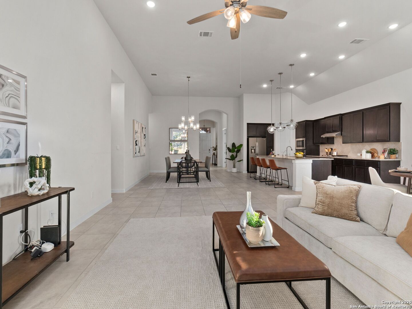 Open living and dining area with a light sofa, dark kitchen cabinetry, and vaulted ceiling.