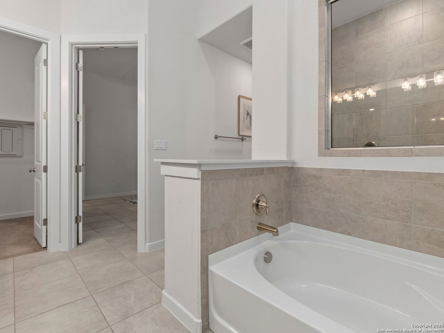 Bathroom with a large soaking tub, beige tiled surround, and wide mirror.