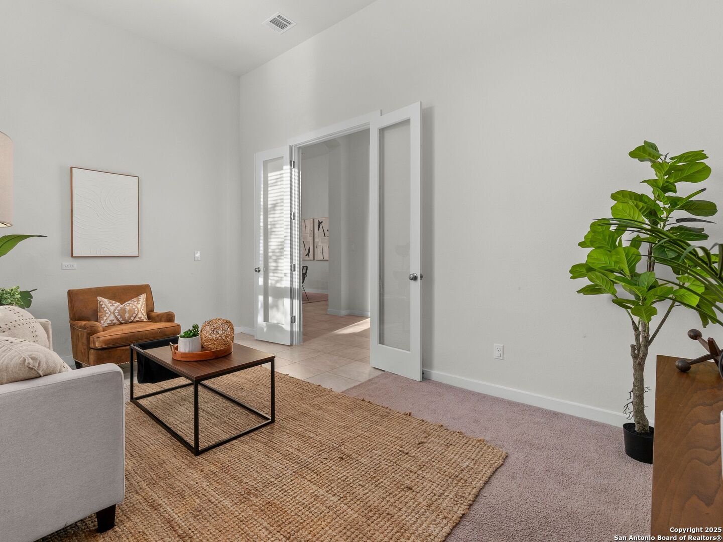 Staged living room with a woven rug, brown leather armchair, and open double doors.